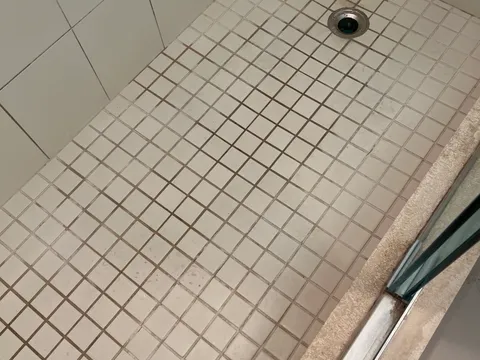 Before: Mosaic shower floor with dark, moldy grout before and bright white grout after cleaning and sealing